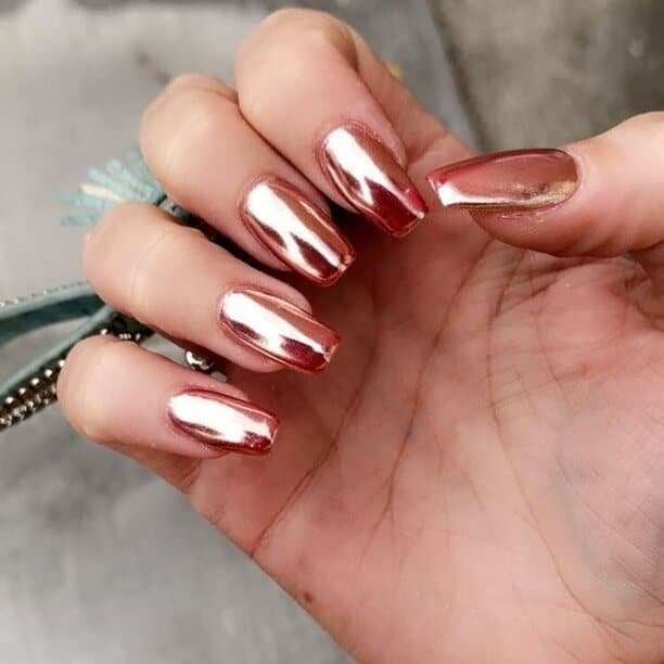 Hands displaying different metallic nail styles, featuring black nails with silver specks, dark gold polish, and shiny red acrylic nails.
