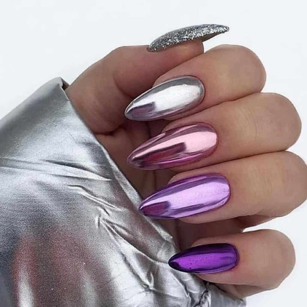 Hands displaying different metallic nail styles, featuring black nails with silver specks, dark gold polish, and shiny red acrylic nails.