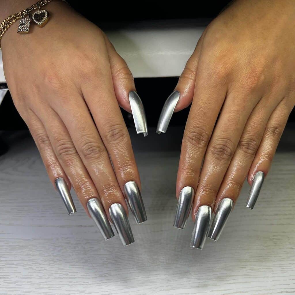 Hands displaying different metallic nail styles, featuring black nails with silver specks, dark gold polish, and shiny red acrylic nails.